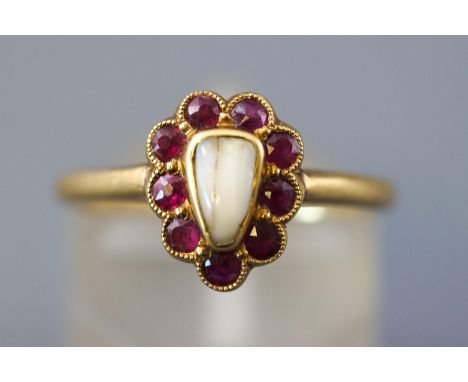 A yellow metal memorial  ring set with a halo of rubies  surrounding a human tooth. Stamped 18ct and shank inscribed 'Nigel' 