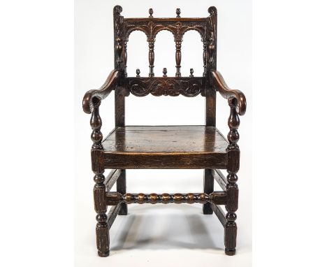 A 17th century oak elbow chair, with open arched back, acorn finials, solid seat and bobbin turned stretcher 96cm high x 57cm