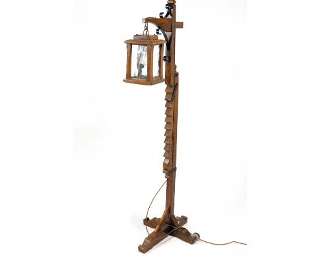 An oak adjustable standard lamp, with glazed lantern suspended from an arm with wrought iron brackets, on an "X" base, height
