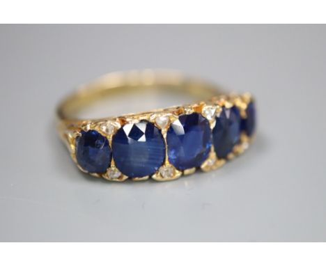 A George V 18ct gold and graduated five stone sapphire set half hoop ring, with diamond chip spacers, size Q/R, gross 5.9 gra