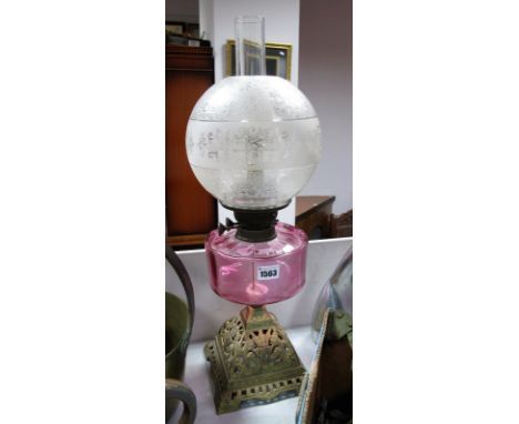 A Circa 1900 Paraffin Lamp, cranberry glass reservoir, on a pierced gilt effect cast iron squared base, acid etched globular 