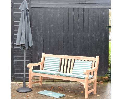 A hardwood garden bench, with white and green striped loose cushions, and cover, 183cm, together with a black parasol on stan