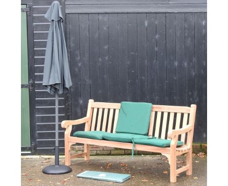 A hardwood garden bench, with green loose cushions, and cover, 183cm, together with a black parasol on stand