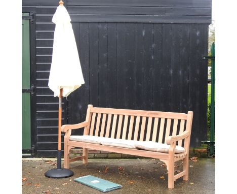 A hardwood garden bench, with cream loose cushions, and cover, 183cm, together with a cream parasol on stand