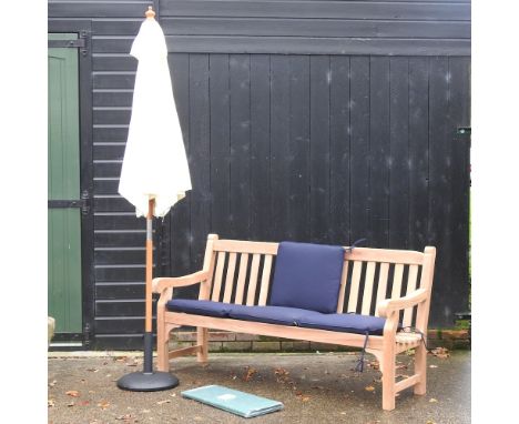 A teak garden bench, with blue loose cushions, and cover, 183cm, together with a cream parasol on stand