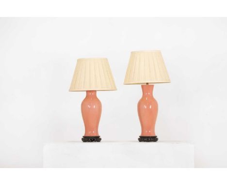 A pair of pink porcelain table lamps,early 20th century, Chinese, each on a wooden stand with a pleated silk shade,36cm high 