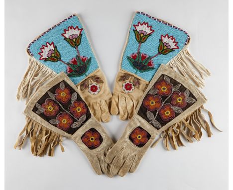 Two pairs of Native American leather gauntlets or gloves with intricately beaded floral motifs and tasseled fringes. One pair