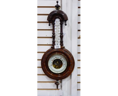 A stained walnut barometer having turned finial to the carved arch above the thermometer, foliate carving surrounding the dia