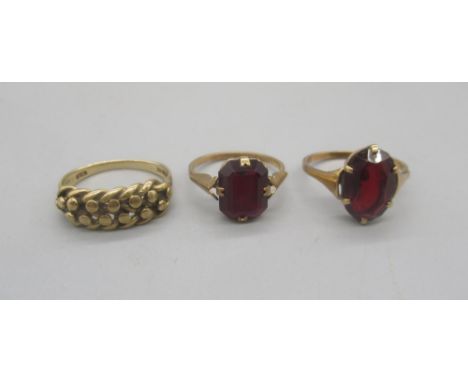 Two 9ct yellow gold rings set with red stones, size N1/2 and K, and a 9ct yellow gold keeper ring, size M1/2, all stamped 375