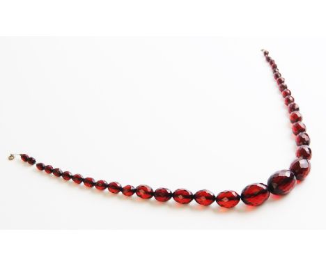 A cherry amber bead necklace, comprising thirty-four graduated faceted beads measuring between 10mm x 8mm and 30mm x 24mm, se