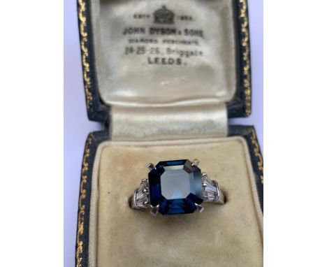 A sapphire and diamond ring, comprising a central octagonal cut blue sapphire weighing approx. 5.6ct approx, with three taper