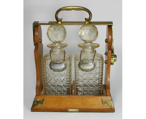 A two division oak and brass mounted tantalus by Betjemann, with a pair of cut glass decanters and stoppers, each with silver