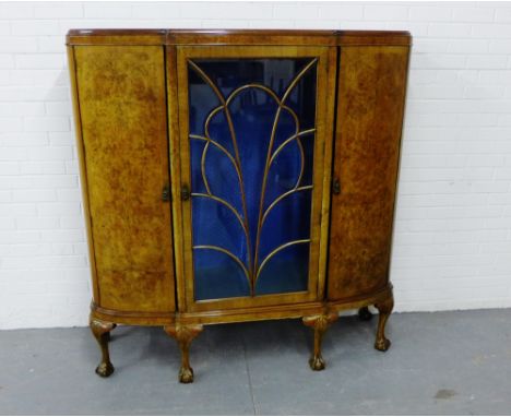 An Art Deco burr walnut display cabinet, with a central glazed panel flanked by a pair of curved cupboard doors, raised on ca