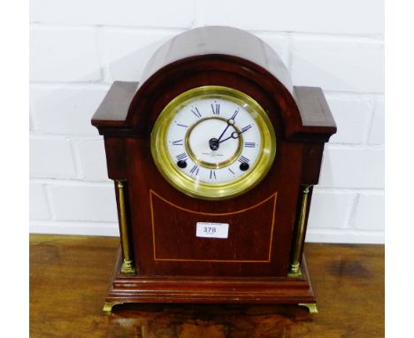 A mahogany and inlaid mantle clock, the domed top over an enamel dial with Roman numerals, flanked by brass columns, on a pli