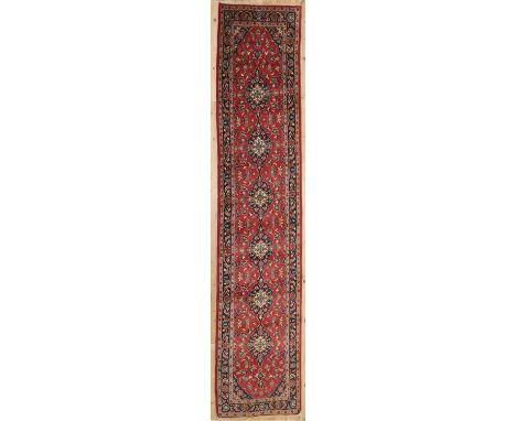 A Persian wool runner, mid-20th century, Kashan, the red field woven with repeating central medallions, 402 x 102 cmCondition