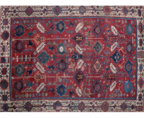 A tribal wool rug, early 20th century, the red field woven with stylised floral and animal motifs, within a geometrically dec