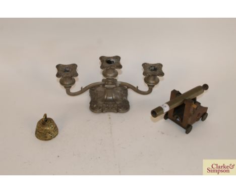 A brass model of a cannon; a small brass bell with embossed decoration and a plated three light candelabra