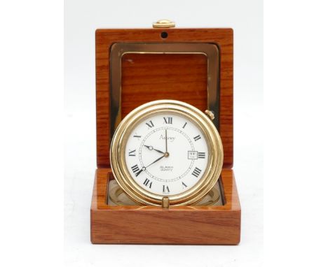 Asprey, a gilt brass circular travel alarm clock with date aperture, synthetic sapphire crown, hours in a mahogany and brass 