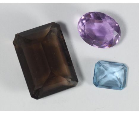 Three various gemstones comprising an amethyst coloured faceted oval stone, a large emerald cut smoky quartz and a scissor cu