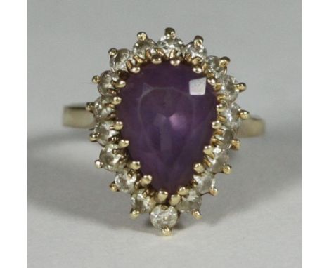 A yellow metal (tests as 14ct gold or above) ring, centrally claw set with a pear cut amethyst coloured stone, surrounded by 