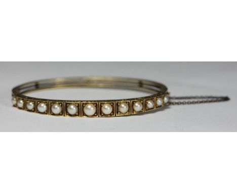 An early 20th century unmarked yellow metal and pearl hinged bangle, (testing as 14ct), set with thirteen graduated blister p