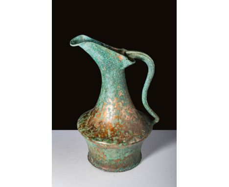 Ca. 500 BC.A bronze oinochoe with a flat base and an upward-flaring lower body. The vessel exhibits a sharp carination that d