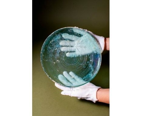 Ca. AD 100 - 300.A glass dish with a rounded base and a broad, shallow body. The rim curves gently inward, while the interior