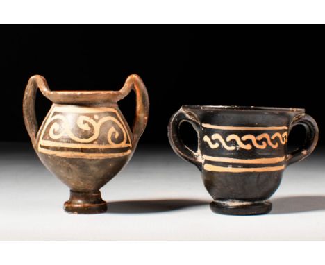 Ca. 400 - 300 BC.A pair of miniature black-glazed pottery vessels. The kantharos has a biconical body elevated on a small cir