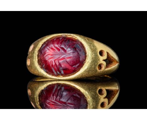 Ca. AD 300.A gold openwork ring, composed of a round hoop that expands at the shoulders to form a round bezel, securing a red