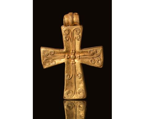 Ca. AD 500 - 700.A hollow gold cross pendant with arms that slightly flare outward. The upper face is adorned with swirling d