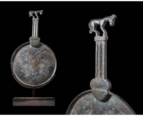 Ca. 600 BC.A bronze mirror with a large, flat circular body, raised borders and a short-tanged column-shaped handle. A standi
