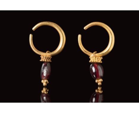 Ca. AD 100 - 300.A pair of gold Roman earrings with large red garnet beads secured by two crowns of gold bead work connected 