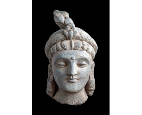 Ca. AD 200 - 300.A schist head of a Bodhisattva with a serene expression, heavy-lidded eyes, and an intricate coiffure surmou
