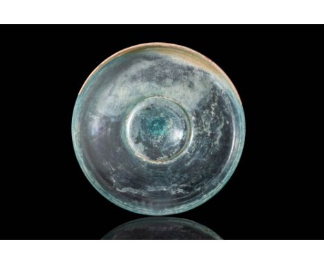 Ca. AD 1 - 100.A glass dish of translucent blue colour with a broad, shallow body resting on a concave, elevated foot, bearin