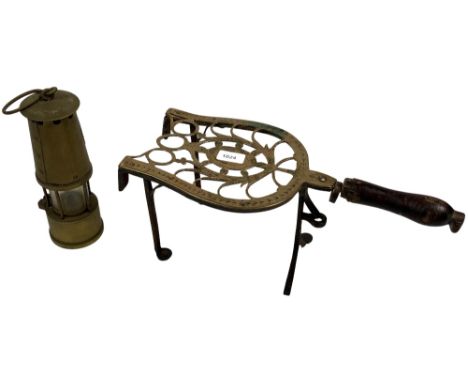 A George III bright cut brass and iron Trivet, with pierced top, wooden handle and iron legs, together with a Protector Lamp 