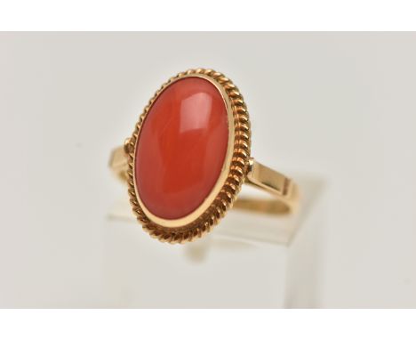 A YELLOW METAL CORAL RING, oval coral cabochon, collet set in yellow metal with rope detail surround, yellow metal shank, sta