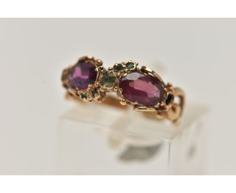 A YELLOW METAL GEM SET VICTORIAN RING, set with two oval cut amethysts and circular cut emerald accents, scrolling shoulders 