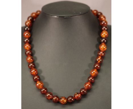 AN AMBER NECKLACE of spherical beads finishing with a white metal ring and T-bar clasp. 52cm, 57grams  CONDITION: Generally g