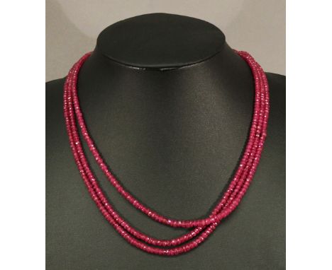 A FACET-CUT RUBY NECKLACE having three strings of multiple facet-cut and graduating stones finishing with a yellow metal loop