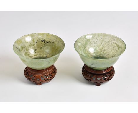 A mottled pair of Chinese spinach green slightly translucent jade bowls, 20th century, the thin rounded sides rising from a s
