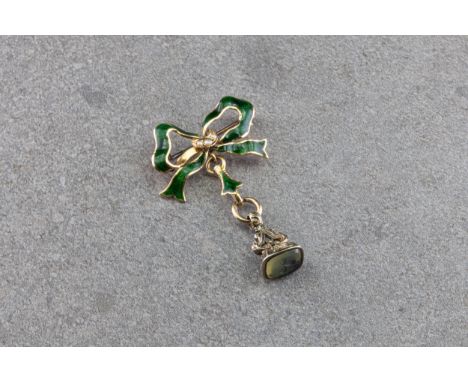 An 18ct gold and enamel bow brooch, the bow decorated with dark green enamel and centred with three seed pearls, suspending a