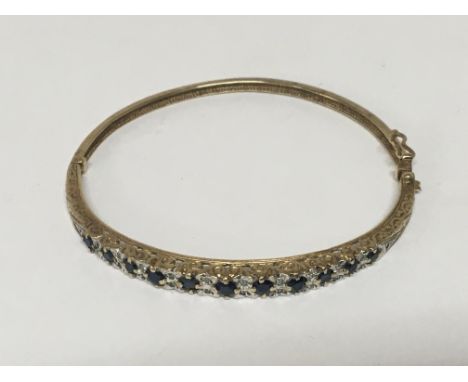A gold bangle set with an alternating pattern of sapphire and diamonds. Weight 11g