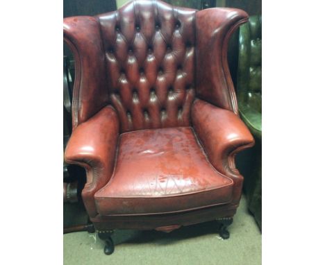 A red leather wing armchair with button back on cabriole legs .