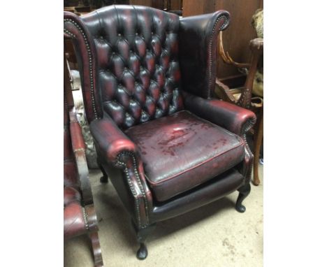 A red leather wing armchair with button back on cabriole cabriole legs .