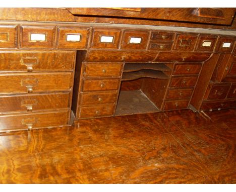 An oak roll top desk, the tambour front enclosing a selection of open compartments and drawers, the whole raised on plinths c