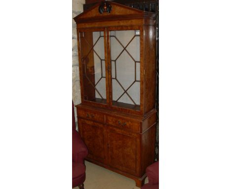 A modern burr elm veneered bookcase cabinet in the Georgian taste, the broken arch pediment above two astragal glazed doors o