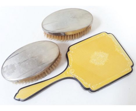 Hallmarked silver comprising a silver and enamel mirror and a pair of silver backed brushes. 