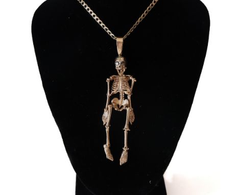 A modern pendant in the form of an articulated skeleton with garnet eyes, on a 9ct gold filed-curb necklace, post 2000 conven