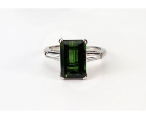 A green tourmaline and diamond three stone ring, claw set to the centre with a rectangular step-cut bright-green tourmaline, 