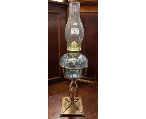 Brass single burner oil lamp with wrythen coloured glass reservoir on a stylised brass pedestal on square base with bun feet,